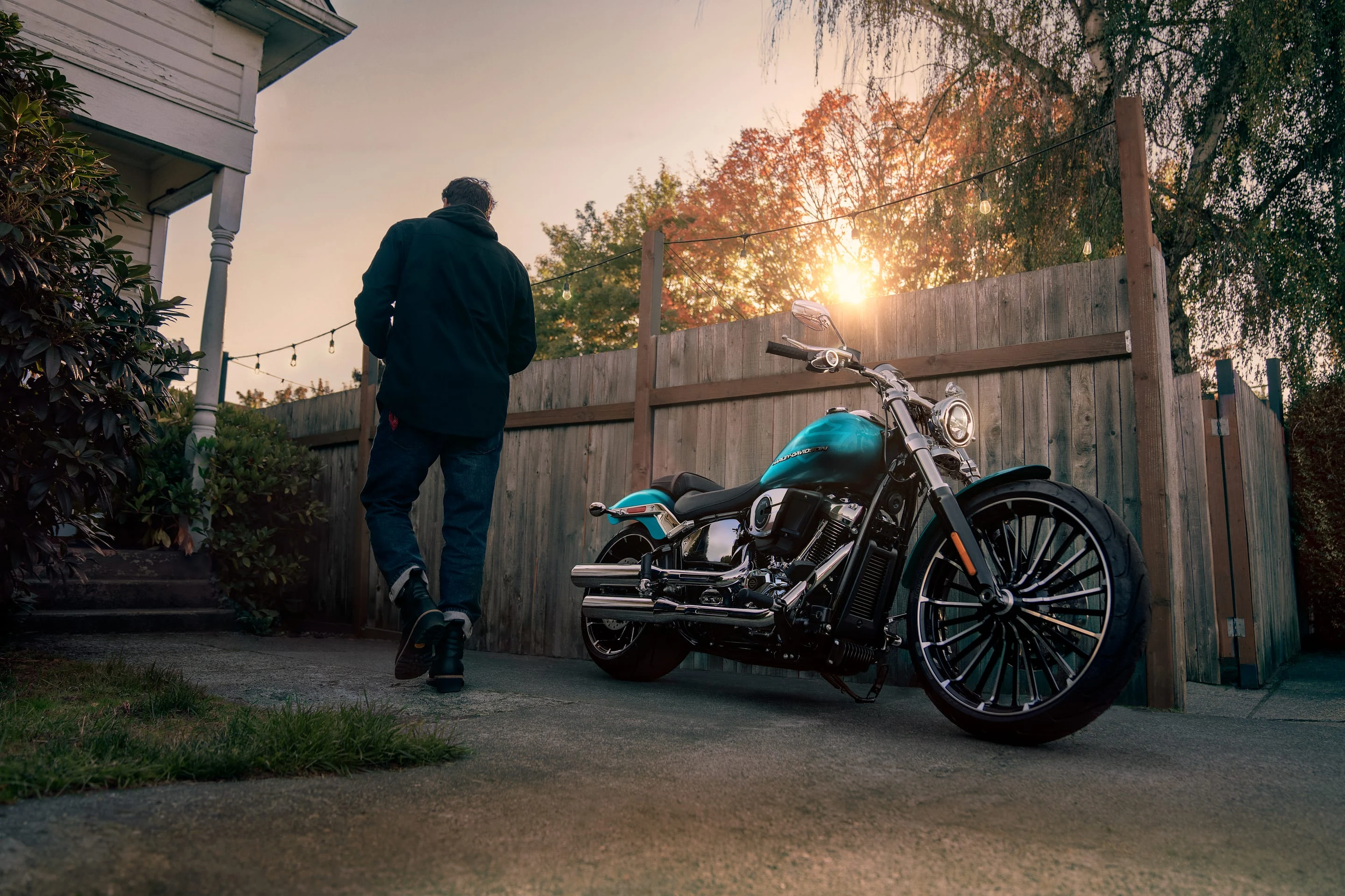 A rider beside a turquoise Harley-Davidson at sunset.